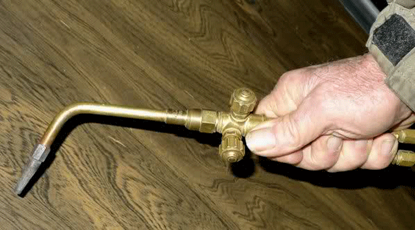 Fig. 2 -- Single-tipped brazing torch. Notice on the right side of the man’s hand that there are two gas inlets into the torch mixer-head. To the left of his hand in the photo are two knobs on the mixer body that can regulate the flow of gas through each of the two gas feeder pipes in the mixer-body he is holding.