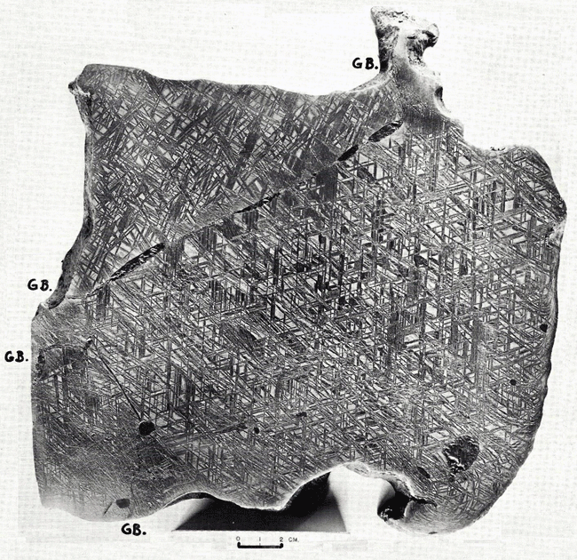 Figure 6: A macroetched slice from Gibeon displaying the original taenite grain boundaries (G.B.) and elongated troilite inclusions (FeS). The lower right corner displays severe plastic deformation possibly caused during the fall. The scale bar below the photograph is 2 cm. Photo courtesy of Dr. Vagn Buchwald [1].